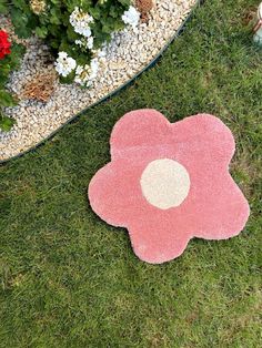 a pink flower rug sitting on top of a lush green grass covered ground next to flowers