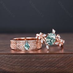 two wedding rings with green and white stones in them on a wooden table next to each other