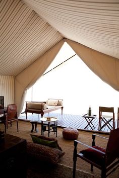 the inside of a tent with chairs, tables and couches in front of it