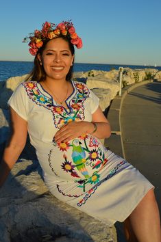 a woman sitting on the edge of a cliff next to the ocean wearing a flower crown