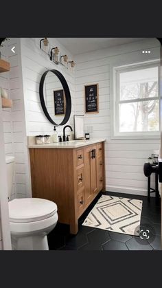 a white toilet sitting next to a wooden vanity in a bathroom under a mirror above a sink