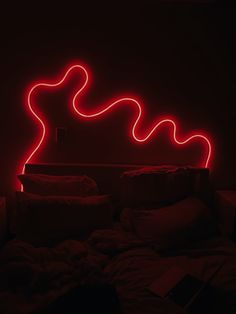 a red neon sign sitting on top of a bed in a dark room with pillows