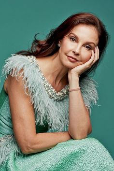 a woman in a green dress is posing for the camera with her hand on her chin