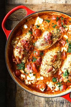 a red pan filled with chicken, tomatoes and cheese on top of a wooden table