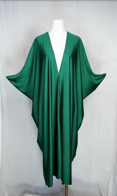 Introducing the Huntress Caftan, a must-have for any fashion-forward individual. This exquisite garment is more than just a piece of clothing; it's a celebration of fabric in all its glory. Crafted with high-quality emerald green jersey and lots of love, this piece offers an airy fit designed to drape beautifully on all body types. Whether worn poolside for a day at the cabana or layered and adorned with your favorite accessories for a glamorous evening affair, it's a versatile wardrobe staple that effortlessly adapts to your every mood and occasion. Bohemian splendor, handmade in California. Our caftans are a voluminous one-size fits all garment, approximately 50" in length. The intention of this shape is to celebrate the magic of fabric and its captivating dance with form. JG one-size ca Bohemian Maxi Dress With Kimono Sleeves For Evening, Bohemian Green V-neck Abaya, Elegant Green Maxi Dress For Festival, Green Long Abaya For Party, Green Long Party Abaya, Elegant Green Maxi Kimono, Elegant Green Maxi-length Kimono, Elegant V-neck Kaftan For Fall, Elegant V-neck Fall Kaftan