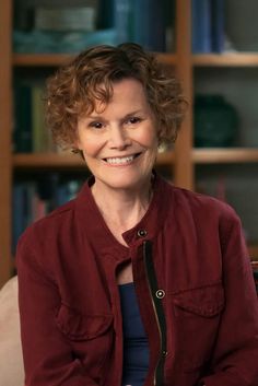 a smiling woman sitting in front of a book shelf