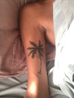 a person laying in bed with a tattoo on their arm that has a palm tree on it