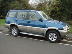 a blue and silver suv parked on the side of a road in front of some trees