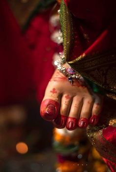 a woman's hand with red and gold paint on it, holding onto her wrist