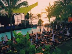 an outdoor swimming pool with people sitting and standing around it at sunset or sunrise time