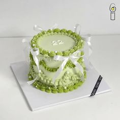 a cake decorated with green icing and white ribbons on top of a book that says twenty