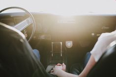 two people sitting in the driver's seat of a car with their hands on the steering wheel