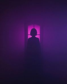 a person standing in front of a window with purple light coming through the room and their shadow on the wall