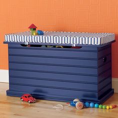 a toy chest sitting on top of a hard wood floor next to a orange wall