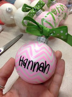 a hand holding a pink ornament with the word hannah on it and green ribbon