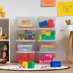 a room filled with lots of toys and plastic bins on the floor next to a book shelf