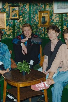 three men sitting at a table in a room with green walls and floral wallpaper