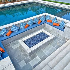 an outdoor seating area next to a swimming pool with blue and orange pillows on it