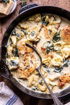 a skillet filled with ravioli and spinach covered in cheese on top of a wooden table