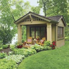 a small garden shed with chairs and flowers in the front yard, next to a lake