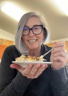 an older woman with glasses holding a plate of food in her hands and smiling at the camera