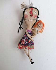 a doll hanging on the wall with an orange hair and black eyeliners holding a stuffed animal