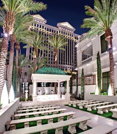 an outdoor dining area with benches and palm trees in front of the hotel at night