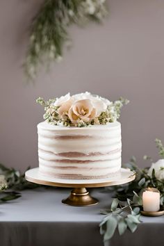 a white wedding cake with flowers and greenery on the top is sitting on a table