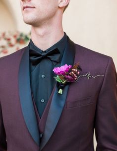 a man wearing a purple suit and black bow tie with a flower in his lapel