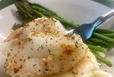 a white plate topped with scallops and asparagus next to a fork