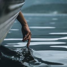 a person reaching for something in the water with their hand on top of a boat