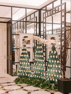 Image of 3 large, printed Christmas trees in an entryway The trees are seating charts where each ornament has the guest name and table number printed. The ornaments are attached to the tree and are removable for guests to take to their seats. Christmas Venue Decorations