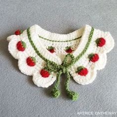 a crocheted white sweater with cherries and green leaves on the collar is sitting on a gray surface