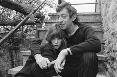 a man and woman sitting on the steps in front of some stairs with their arms around each other