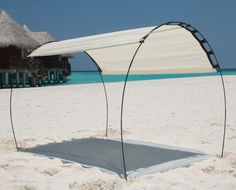 an empty bed on the beach in front of some water and thatched umbrellas