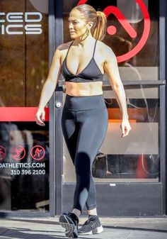 a woman in black sports bra top and leggings walking down the street with her hand on her hip