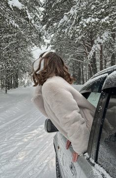 a woman standing next to a car on a snowy road in the snow with trees behind her