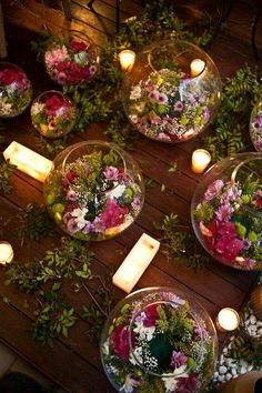 flowers and candles are arranged in glass bowls on a table surrounded by greenery, rocks and candles