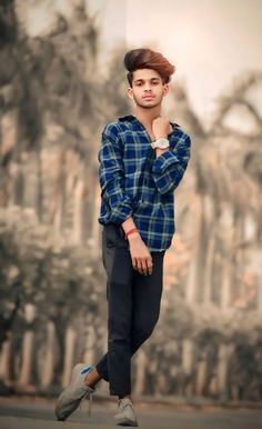 a young man standing in front of a wall with his hand on his chin and looking at the camera