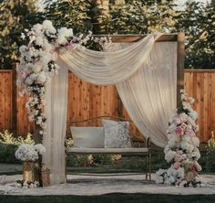 an outdoor wedding ceremony setup with flowers on the arch and white drapes draped over it