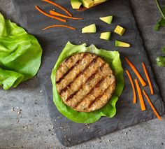 a burger with lettuce and carrots on a slate board next to some cut up vegetables