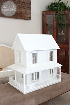 a white doll house sitting on top of a table next to a couch and chair