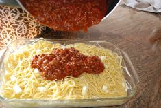 spaghetti and sauce in a glass dish on a wooden table next to a pot of pasta