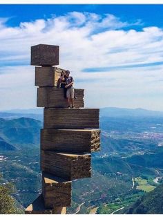 two people standing on top of a wooden structure with mountains in the background and blue sky