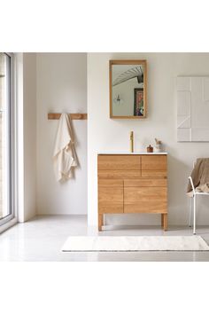 a white bathroom with a wooden cabinet and mirror on the wall next to a chair