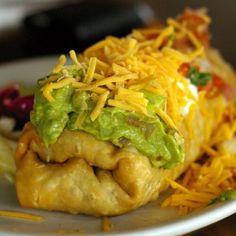 an enchilada with cheese and guacamole on it sits on a plate