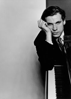 a black and white photo of a man leaning on a piano with his hands to his face