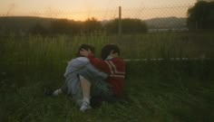 two people sitting in the grass with their backs to each other as the sun sets