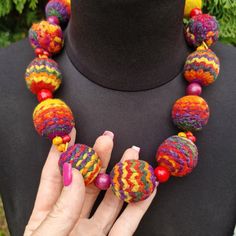 a woman's hand holding a multicolored necklace on a mannequin