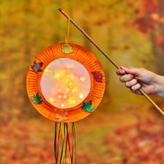 a hand holding a stick and an orange paper plate with flowers on it, in front of a fall background